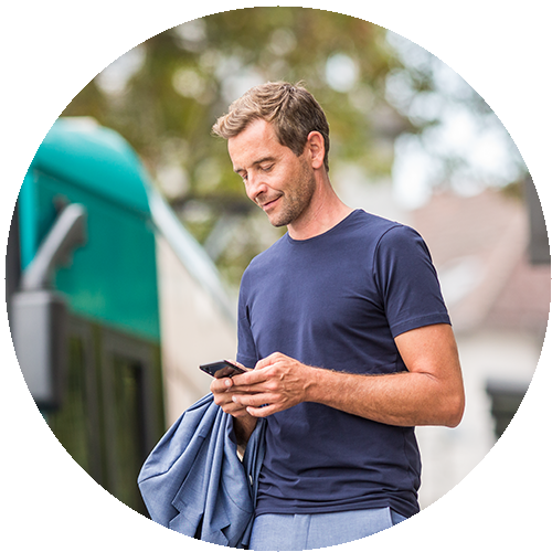 Ein Mann steht an einer Straßenbahnhaltestelle und betrachtet sein Smartphone