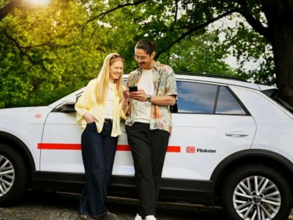 Zwei Personen vor einem Flinkster-Fahrzeug.