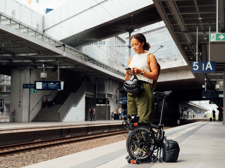 Frau mit zusammengeklappten Brompton Electric C Line am Bahnsteig.